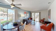This single-floor residence offers three bedrooms and two bathrooms thoughtfully arranged within a compact yet functional layout. Light wood-style flooring flows throughout the home, lending a cohesive and clean aesthetic to every room.

The open-concept living and dining area serves as the heart of the home, anchored by a striking slate-blue accent wall and sliding glass doors that invite natural light and provide views of the surrounding outdoor area. Ceiling fans in both the living and dining spaces enhance comfort and airflow. The dining area is positioned near large windows, offering additional natural light and outdoor views.

The galley-style kitchen is efficiently designed with warm wood cabinetry, white countertops, a gas range, and a stainless steel refrigerator, making practical use of the available space.

The primary bedroom is a comfortable retreat featuring wood-style flooring, a dedicated closet with built-in shelving, and access to an adjacent vanity area. The bathrooms are clean and functional, each featuring a tub-shower combination with chrome fixtures.

A dedicated closet with built-in shelving rods provides convenient storage. Throughout the residence, a textured ceiling, neutral walls, and consistent flooring create a unified and inviting atmosphere suited for everyday living.
