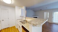 Located at 303 Sunchase Blvd in Farmville, Virginia, this single-story residence offers a thoughtfully designed open-concept layout that connects the kitchen and living areas seamlessly. The kitchen is a functional highlight of the home, featuring white cabinetry, light granite countertops, a double stainless steel sink, and a peninsula that extends into the living space, providing additional prep and seating opportunities. Stainless steel appliances, including a refrigerator, range, and microwave, complete the kitchen. The living area is anchored by a corner fireplace and benefits from vaulted ceilings that lend an airy, open quality to the space. Wood-look flooring runs throughout the main living and kitchen areas, while the bedrooms are finished with plush carpeting for added comfort. Each bedroom includes a ceiling fan with light, natural light from windows with blinds, and closet storage. One bedroom features a vaulted ceiling detail, adding architectural interest. The bathrooms are clean and straightforward, each equipped with a tub-shower combination, chrome fixtures, and light tile flooring. One bathroom includes a white vanity with additional storage. Overall, the home presents a bright, neutral palette throughout.