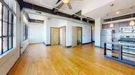 This urban loft-style unit at 101 East 6th Street blends industrial character with modern finishes. The open living area impresses with hardwood floors, exposed structural beams, visible ductwork, and oversized factory-style windows that flood the space with natural light and offer sweeping city views. Ceiling fans enhance comfort throughout. The kitchen features rich dark wood cabinetry, granite countertops, stainless steel appliances, and a breakfast bar. Both bedrooms continue the hardwood flooring and industrial aesthetic, with the primary bedroom offering dual closets with built-in shelving. The full bathroom includes a tub-shower combo with clean, neutral finishes.