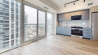 Located in Toronto, ON, this thoughtfully designed 2-bedroom, 2-bathroom unit offers a clean, contemporary aesthetic throughout. Light hardwood flooring runs continuously across the living areas and bedrooms, complementing the crisp white walls and creating a bright, cohesive interior.

The open-concept living area and kitchen are anchored by expansive floor-to-ceiling windows and sliding glass doors that frame sweeping views of the Toronto skyline, flooding the space with natural light. The kitchen features modern flat-panel cabinetry in a muted blue-grey tone, integrated appliances, and track lighting overhead.

Both bedrooms are well-proportioned, with large windows offering elevated city views. The primary bedroom includes sleek sliding closet doors with glossy white panels and black frames, and direct access to the private balcony. The second bedroom benefits from generous natural light and connects seamlessly to the hallway.

The two bathrooms are finished with large-format marble-effect porcelain tiles from floor to ceiling, lending a polished, upscale feel. One bathroom features a soaking tub with a tub-filler fixture, while the other offers a glass-enclosed walk-in shower. A hallway connects all rooms efficiently, completing this well-appointed urban residence.