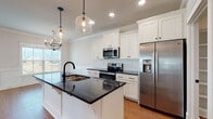 This single-floor home offers a thoughtfully designed open-concept layout that seamlessly connects the kitchen, dining, and living areas. The kitchen is a standout centerpiece, featuring crisp white shaker-style cabinetry with matte black hardware, dark granite countertops, a classic white subway tile backsplash, and a generous island with an undermount sink and matte black faucet. Stainless steel appliances, including a French door refrigerator with ice dispenser and an electric range with over-the-range microwave, complete the culinary space. Seeded glass pendant lights add a warm, contemporary touch overhead.

The open living area flows naturally from the kitchen and is anchored by a sleek electric fireplace set within a crisp white paneled surround. Crown molding, wainscoting, and warm hardwood-style flooring run consistently throughout, lending a polished and cohesive aesthetic. Recessed lighting and ceiling fans provide both function and comfort.

The bathroom features a double-sink vanity with granite countertops, white shaker cabinetry, and warm wall sconces. A dedicated laundry room includes a full-size washer and dryer with overhead cabinetry for added storage. Bedrooms are bright and open, accented with shiplap detailing and barn-style doors, completing this well-crafted home.