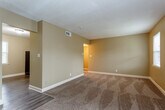 Located at 6102 Foster St in Overland Park, Kansas, this single-story space offers a functional and comfortable layout with a consistent design aesthetic throughout. Warm beige-toned walls and textured ceilings are present across the living areas, creating a cohesive and neutral backdrop suited to a variety of furnishing styles.

The main living area is generously sized, featuring plush wall-to-wall carpeting and a striking full brick accent wall that serves as a distinctive architectural focal point. The open layout connects seamlessly to an additional carpeted room, which benefits from multiple windows allowing natural light to filter in, along with a sliding glass door fitted with vertical blinds that offers views of the outdoors.

The bedrooms are carpeted and well-proportioned, each with windows fitted with blinds providing natural light and privacy. The kitchen is thoughtfully appointed with rich dark wood cabinetry, granite-style countertops, a double-basin sink, and black appliances including a dishwasher and range, all set over durable wood-look flooring.

The bathroom features a white vanity, a tiled tub-shower combination, and a window that introduces natural light. Overall, the space presents a practical and inviting single-floor layout with character details throughout.