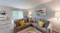 This single-floor residence at Cowesett Hills Apartments in Warwick, Rhode Island is thoughtfully laid out to maximize comfort and functionality. The living room serves as the central gathering space, featuring plush carpeting, neutral walls, and a large sliding glass door fitted with vertical blinds that opens to an outdoor balcony, allowing generous natural light and views of surrounding greenery.

The kitchen is well-appointed with warm wood cabinetry, granite countertops, a gas range, dishwasher, and tile flooring, providing ample workspace for cooking. Adjacent to the kitchen, the dining area accommodates a full-sized table and receives natural light through a window with vertical blinds, complemented by a wall-mounted air conditioning unit.

The bedrooms are carpeted and comfortable, each featuring closet storage and windows that invite natural light. One bedroom includes a sliding closet with shelving, while another offers access to additional storage. The bathroom features wood-look vinyl flooring, a vanity with cabinet storage, a well-lit mirror, and a shower-tub combination. Throughout the residence, a consistent neutral color palette and carpet flooring create a cohesive and welcoming ambiance suited for everyday living.