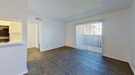 This efficiently designed one-bedroom, one-bathroom unit offers a practical single-floor layout across a compact but well-utilized footprint. The living room serves as the central gathering space, finished with dark hardwood-style flooring and anchored by a large sliding glass door dressed with vertical blinds, allowing generous natural light and outdoor views. A textured ceiling and crisp white walls carry throughout the unit, lending a clean, consistent aesthetic.

The galley-style kitchen runs parallel to the living area and features white cabinetry with simple bar-pull hardware, light stone-look countertops, a stainless steel sink, and black appliances including a coil-burner range with overhead exhaust and a full-size refrigerator. The layout is narrow but functional, with ample cabinet storage on both sides.

The bedroom is carpeted and comfortably proportioned, featuring a large window with horizontal blinds that provides natural light and exterior views. A ceiling fan with integrated lighting adds comfort and functionality. The bedroom also includes access to a closet.

The bathroom is finished in white with a stone-look vanity countertop, white cabinetry, and a full tub-shower combination. A hallway connects the rooms, completing the straightforward and efficient layout.