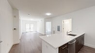 This well-appointed single-floor residence showcases a clean, contemporary design with crisp white walls and warm wood-look flooring carried consistently throughout the space. The open-concept kitchen is a standout feature, equipped with rich dark-wood cabinetry, stainless steel appliances including a gas range, microwave, and refrigerator, a mosaic tile backsplash, and an expansive white quartz island with an integrated sink — ideal for both cooking and entertaining. The kitchen flows seamlessly into a generous living area that benefits from natural light streaming through large French doors leading to an outdoor area. The bedrooms are bright and spacious, each featuring large windows that invite abundant natural light and views of the surrounding neighborhood. Ample closet space, including a walk-in closet, adds to the practicality of the layout. The bathrooms are finished with light tile flooring, white subway tile surrounds accented by a dark mosaic border, white quartz vanity countertops, and dark wood vanity cabinetry. A dedicated electrical panel and in-unit utility access further enhance the functionality of this thoughtfully designed residence. The overall ambiance is modern, clean, and move-in ready.