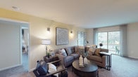 Durham Woods 2M is a single-floor residence that blends comfortable living with a cohesive, neutral aesthetic throughout. The living room serves as the heart of the home, featuring plush carpeting, warm wall-mounted lighting, and large windows that invite an abundance of natural light while offering pleasant outdoor views. The open layout accommodates both a generous seating arrangement and a dedicated workspace area, making the space as functional as it is inviting.

The kitchen is outfitted with warm oak cabinetry, granite-style countertops, tile flooring, and a full suite of white appliances including a gas range and dishwasher. It connects directly to a separate dining area, which features tile flooring, a statement pendant light, and a cozy round dining table framed by elegant framed artwork.

The bedrooms are carpeted and well-sized, offering ample room for varied configurations. One bedroom showcases a nature-inspired birch tree accent wall paired with large windows, creating a serene retreat. Another bedroom provides a calm, neutral setting ideal for rest or a personal sanctuary.

The bathroom is clean and functional, featuring a vanity with warm wood cabinetry, a white countertop, and tile flooring. Throughout the residence, a consistent warm, neutral palette and tasteful décor create a welcoming and polished ambiance.