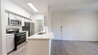 This single-story, 3-bedroom, 2-bathroom home offers a thoughtfully designed layout with modern finishes throughout. The combined kitchen and living area serves as the heart of the home, featuring a peninsula with a white quartz countertop and undermount sink, stainless steel appliances including a refrigerator, range, and over-the-range microwave, white cabinetry, and a tile backsplash. A skylight above the kitchen fills the space with natural light, while wood-look vinyl plank flooring extends throughout the main areas. The primary bedroom is a comfortable size and includes two closets, providing ample storage. A sliding glass door opens to an outdoor view, complemented by a ceiling fan and crown molding. The secondary bedrooms feature plush carpet, ceiling fans, and windows that allow in natural light. Four closets are distributed across the home, ensuring generous storage options. Both bathrooms are finished with white cabinetry, quartz countertops, framed mirrors, and tiled tub-shower combinations. A dedicated laundry room includes built-in shelving, a window, and utility hookups. The clean, neutral color palette and consistent modern finishes give the entire home a bright, cohesive ambiance.
