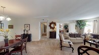 This single-story residence offers three bedrooms and two full bathrooms within a well-organized, generously sized floor plan. The living room serves as the heart of the home, featuring plush carpeting, multiple windows that invite natural light, and ample space for flexible furniture arrangements. It opens naturally toward the dining area, which is highlighted by a classic chandelier and carpeted flooring, creating an inviting setting for everyday meals or entertaining.

The galley-style kitchen is efficiently designed with white cabinetry, white appliances, a double sink, and light tile flooring. A window above the counter area provides additional natural light. The layout maximizes storage and counter space within a compact, streamlined footprint.

The primary bedroom is spacious with plush carpet, two windows, a ceiling fan, and generous closet space, including a walk-in closet. The accompanying primary bathroom features a vanity with white cabinetry, an ornate mirror, and a shower-tub combination. The second bathroom mirrors a similar layout with tile flooring, a tub-shower combo, and a well-lit vanity. Throughout the home, neutral wall tones and carpet create a cohesive, understated aesthetic that is both functional and comfortable.