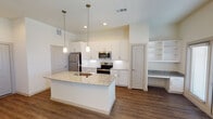 Located in Waxahachie, TX, this single-story home showcases a clean, contemporary design with consistent wood-look flooring and neutral tones throughout. The heart of the home is an open-concept kitchen outfitted with crisp white shaker cabinetry, a white subway tile backsplash, and granite countertops that extend across a central island with an undermount sink. Stainless steel appliances — including a refrigerator, electric range, and built-in microwave — complete the space, while pendant lighting above the island adds a refined touch. Adjacent to the kitchen is a convenient built-in desk nook with open shelving, ideal for a home office or study area. The living areas feature high ceilings that enhance the sense of openness and are bathed in natural light through multiple windows dressed with blinds. Ceiling fans are present in the bedrooms, which also benefit from natural light and generous proportions. The primary bedroom includes access to a walk-in closet and a private bathroom. The bathroom is appointed with a granite-topped vanity, a soaking tub, and a full marble-tile surround, creating a polished and relaxing retreat. Throughout the home, thoughtful finishes and a cohesive color palette lend a move-in-ready appeal.