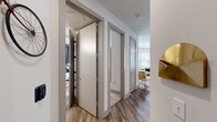 Located in Dallas, TX, this one-bedroom, one-bathroom residence offers a thoughtfully designed open-concept layout. Wood-style flooring flows throughout the main living areas, connecting the living room, dining area, and kitchen seamlessly. The living room features large windows with horizontal blinds and grommet curtains that flood the space with natural light, complemented by a ceiling fan and a bold geometric accent wall. The dining area sits adjacent to the living room, benefiting from the same generous window coverage. The galley-style kitchen is well-equipped with dark wood cabinetry, white quartz countertops, a subway tile backsplash, stainless steel appliances, and pendant lighting over a kitchen island. A hallway with modern gray-trimmed doors leads to the private spaces, including the bedroom, bathroom, and closet. The bedroom features plush carpeting, a striking blue accent wall, a ceiling fan, and French doors that open to the outdoors. A dedicated closet provides organized storage. The bathroom offers dark wood vanity cabinetry, a white countertop, a large mirror, and a full shower-tub combination with wood-style flooring continuing throughout.
