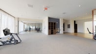 Located at 8390 NW 53rd St in Doral, FL, this professionally equipped fitness center offers a comprehensive, single-floor layout designed to support a full range of workout activities. The space is organized into distinct functional zones, each thoughtfully appointed for a specific training purpose.

The cardio area features a row of modern treadmills and elliptical machines positioned directly in front of floor-to-ceiling windows draped with sheer curtains, allowing abundant natural light and open outdoor views to enhance the workout experience. Adjacent to this zone, a strength training area houses a multi-station cable machine, weight benches, free weights, and additional resistance equipment, all arranged on durable rubberized flooring.

A dedicated indoor cycling studio is enclosed by glass partitions framed in warm wood, providing visual separation while maintaining an open feel. The studio is lined with spin bikes and mirrors that amplify the sense of space.

The flex or studio area features light hardwood flooring and clean white walls accented by a bold charcoal feature wall, making it suitable for group fitness classes or stretching. A locker corridor with built-in white lockers, wood-toned bench seating, and hardwood floors connects the various zones and provides convenient storage. Wooden shelving units and a water station add practical amenities throughout.