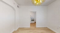 Located at 1663 E Ninth St in Tucson, AZ, this efficiently designed one-bedroom, one-bathroom unit offers a clean, modern aesthetic throughout its single floor. Light wood laminate flooring runs continuously across all rooms, creating a cohesive and airy feel. The living room serves as the heart of the unit, highlighted by a bold gold sunburst chandelier that adds a striking design focal point. An arched doorway connects the living area to the rest of the unit, adding a subtle architectural charm. Natural light filters in through window blinds, keeping the all-white interior bright and open. The kitchen is thoughtfully laid out with white cabinetry featuring black hardware, a white gas range, light countertops, and a matte black faucet at the sink — delivering a crisp, contemporary contrast. The bedroom is a cozy, well-proportioned space with a window that brings in natural light. The bathroom continues the modern theme with a glass-panel shower enclosure framed in black, a white vanity, a round mirror, and matte black fixtures that tie the design together cohesively. The overall ambiance is clean, minimal, and move-in ready.