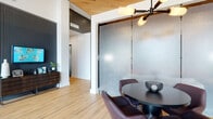 Located at 8601 Anderson Mill Rd in Austin, TX, this single-floor leasing office delivers a polished, contemporary experience from the moment guests arrive. The entry foyer impresses with soaring vaulted ceilings, floor-to-ceiling black-framed glass doors and windows that flood the space with natural light, and warm light wood flooring that carries throughout. Red accent benches flank the entrance, offering a welcoming first impression.

Beyond the entry, the open layout unfolds into a series of distinct yet connected zones. A central lounge area features a neutral sofa with colorful throw pillows, a low coffee table, and curated accent furniture, all framed by dramatic frosted glass partition panels that diffuse light while providing a sense of privacy. A dedicated dining-style meeting nook with a round black table and upholstered swivel chairs sits beneath a striking multi-arm pendant light, accented by a warm wood ceiling detail above.

A cozy banquette alcove offers additional seating with patterned upholstered panels, globe pendant lighting, and a mix of colorful ottomans and lounge chairs, creating an inviting space for casual conversation. The space also includes a well-appointed coffee bar station featuring dark quartz countertops, white cabinetry, and deep blue tile backsplash. Dark accent walls and vertical slat paneling add depth and contrast throughout, completing this sophisticated and functional environment.
