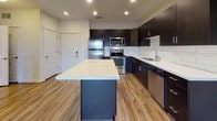 This well-appointed single-floor residence offers a thoughtfully designed layout that balances modern aesthetics with everyday functionality. The kitchen serves as a standout feature, showcasing dark espresso cabinetry that contrasts sharply against bright white quartz countertops and a classic white subway tile backsplash. A generously sized center island provides additional prep and dining space, while a full suite of stainless steel appliances — including a range, microwave, refrigerator, and dishwasher — completes the contemporary look. Warm wood-look flooring runs throughout the kitchen and living areas, adding a natural, inviting tone to the space. Recessed lighting illuminates the kitchen with clean, even light. The bedroom is finished with plush wall-to-wall carpeting for comfort underfoot, and features a ceiling fan with integrated lighting. A wide window allows natural light to filter in, offering a view of the surrounding exterior. The bathroom is cleanly appointed with a dark vanity cabinet topped with a white countertop, a large mirror, and a full-size soaking tub with an overhead shower. Tile flooring adds a polished finish. Overall, the unit presents a cohesive modern design with a neutral, versatile color palette throughout.