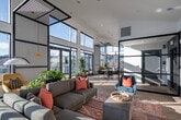 Located at 2124 W Meeker St in Kent, Washington, this single-floor space is defined by its striking architectural character and vibrant, eclectic interior design. The layout encompasses several distinct areas that flow seamlessly into one another, unified by light hardwood flooring throughout.

The main lounge area is immediately impressive, featuring dramatically vaulted ceilings and an expansive wall of floor-to-ceiling black-framed windows that flood the space with natural light and frame open outdoor views. A modern linear fireplace anchors one wall, complemented by a large wall-mounted display, while bold artwork, a large sectional sofa, and vivid accent rugs contribute to the space's energetic aesthetic. A large glass partition wall with black steel framing elegantly separates areas while preserving visual openness.

The dining area benefits from double-height clerestory windows and French doors leading to an outdoor terrace, creating an airy, sun-drenched atmosphere. Potted plants add a natural element beside a round dining table and woven seating.

A separate lounge nook takes on a distinct music-inspired character, featuring an exposed dark brick accent wall, bold yellow pendant lighting, tufted leather seating, music-themed artwork, and a built-in kitchenette. Together, these areas create a dynamic, design-forward space with a cohesive modern-eclectic identity.