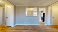 This single-floor space offers a clean, updated interior with a cohesive design carried throughout each room. Wide-plank hardwood flooring runs continuously across the living areas and bedrooms, lending warmth and visual continuity to the layout. Crown molding accents the ceilings in multiple rooms, adding a refined architectural touch alongside crisp white baseboards that frame each space neatly.

The living and dining areas are connected by an open flow, with a distinctive pass-through window that links directly to the kitchen, enhancing the sense of openness. The kitchen is well-equipped with white shaker-style cabinetry, dark granite countertops, a black electric range, and a stainless sink beneath a natural-light window — a practical and attractive space for cooking.

The bedrooms are generously proportioned with neutral gray walls, ample natural light from double-hung windows, and baseboard heating. The bathroom is a standout feature, showcasing large-format stone-look tile on both the floor and the walk-in shower surround, paired with a deep shower base and a window for ventilation and light.

Throughout the space, the neutral gray palette, white trim, and natural wood tones create a calm, modern atmosphere that is both functional and inviting.