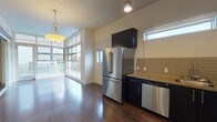 This well-appointed single-floor residence showcases a thoughtfully designed open-concept layout that seamlessly connects the kitchen and living areas. Rich dark hardwood flooring flows throughout the main spaces, providing a striking contrast to the warm, neutral-toned walls.

The kitchen is a standout feature, outfitted with sleek dark cabinetry, granite countertops, and a full suite of stainless steel appliances including a French door refrigerator, gas cooktop, wall oven, built-in microwave, and dishwasher. A classic subway tile backsplash adds texture and visual interest to the culinary space.

The living area benefits from dramatic floor-to-ceiling windows that invite abundant natural light and provide views to an outdoor balcony, creating an airy and open ambiance. The bedroom offers a tranquil retreat with dark hardwood flooring, a horizontal clerestory window for added light and privacy, and a sleek sliding mirrored closet door that enhances the sense of space.

The bathroom is finished with clean white tile, a granite-topped vanity with dark cabinetry, and a full tub and shower combination enclosed by sliding glass doors. Throughout the unit, modern fixtures and a cohesive design palette create a refined, contemporary living environment.