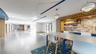 Located at 646 W Bay St in the heart of Savannah, Georgia, this single-floor commercial space offers a thoughtfully designed, open-plan environment suited for dynamic work and collaboration. Polished concrete floors stretch throughout the expansive interior, reflecting natural light that pours in through large windows and glass doors along the perimeter, creating a bright and airy atmosphere.

A distinctive blue accent band curves along the ceiling, adding a bold architectural detail that visually unifies the space. Structural columns with warm wood bases punctuate the floor plan, lending character while defining areas naturally. Private pod-style seating units with vibrant red cushions and teal accent walls offer semi-enclosed nooks ideal for focused work or small meetings.

At one end, a stylish communal area features a high-top table with modern chairs, a decorative geometric-tiled feature wall, and warm pendant lighting — providing an inviting social or collaborative hub. Lounge seating with colorful modular furniture is arranged throughout, complemented by patterned area rugs that add texture and warmth to the industrial aesthetic.

Multiple access points, including glass-paneled entry doors, connect to outdoor areas. The space also includes partitioned rooms along the edges for private use, making it a versatile, well-appointed commercial environment.