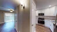 Located at 35995 Fremont Blvd in Fremont, California, this single-floor residence offers a well-designed layout with modern finishes throughout. The kitchen is a standout feature, outfitted with crisp white shaker cabinetry, stainless steel appliances including a gas range, microwave, and dishwasher, and a light-toned countertop that extends into a peninsula — ideal for casual dining or additional prep space. Recessed lighting and wood-look flooring complete the kitchen's clean, contemporary aesthetic. The open living area flows naturally from the kitchen, featuring the same wood-look flooring, recessed lighting, and a ceiling fan for added comfort. Neutral-toned walls and wide baseboards contribute to a bright, airy atmosphere throughout the main living spaces. The bedroom is generously sized with plush wall-to-wall carpeting, a ceiling fan with light fixture, and a large window with blinds that invites natural light and outdoor views of lush greenery. The bathroom is neatly appointed with a vanity featuring a granite-style countertop, a large mirror, a combined tub and shower with a curtain rod, and a high transom window that provides natural light while maintaining privacy. A warmly lit hallway connects the spaces, accented by a decorative wall sconce and textured walls that add subtle character to the home.