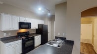 Located at 790 Emory Valley Road in Oak Ridge, Tennessee, this single-floor unit offers a functional and cohesive layout designed for comfortable everyday living. The galley-style kitchen is a standout feature, showcasing crisp white raised-panel cabinetry, dark granite-style countertops, and a full suite of black appliances including a coil-top range, over-the-range microwave, refrigerator, and dishwasher. A double stainless steel sink sits along the kitchen peninsula, and wood-look flooring runs the length of the kitchen corridor, leading toward a window that brings in natural light. The open living area is finished with wall-to-wall carpet, crown molding, and a ceiling fan with integrated lighting. An exterior door in the living space provides direct outdoor access. The bedroom connects to the living area through an elegant arched doorway and includes a closet with sliding doors. The bathroom is well-appointed with a single-sink vanity topped with dark counters, a large mirror with Hollywood-style lighting, a tub-shower combination with tile surround, and wood-look flooring. Neutral warm-toned walls throughout create a cohesive and inviting atmosphere across the entire unit.