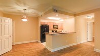 This single-floor space offers a welcoming, open-concept layout that seamlessly connects the kitchen and living areas, creating a sense of spaciousness and ease of movement throughout. The kitchen is a standout feature, equipped with light wood cabinetry that adds warmth to the space, complemented by dark granite countertops that provide both elegance and durability. A breakfast bar peninsula serves as a natural divider between the kitchen and the adjoining living area, making it ideal for casual dining or entertaining. Modern black appliances, including a refrigerator with an ice and water dispenser and an over-the-range microwave, complete the kitchen's functional appeal. Recessed lighting throughout the kitchen ensures bright, even illumination, while a stylish pendant light fixture hangs gracefully in the dining area, adding a decorative touch. The flooring throughout is warm-toned hardwood, providing a cohesive and classic look that ties the entire space together. Crown molding along the ceilings adds a refined architectural detail, and the soft, warm-toned walls contribute to an inviting ambiance. Ample wall outlets and well-placed HVAC vents speak to the thoughtful, practical design of this comfortable and well-appointed space.