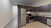 Located at 405 W Redwood Street in Baltimore's vibrant downtown corridor, this two-floor residence showcases a clean, modern aesthetic throughout. The main level features a well-appointed kitchen with dark espresso shaker-style cabinetry, granite countertops, and a full suite of stainless steel appliances, including a refrigerator, electric range, over-the-range microwave, and dishwasher. Light wood-look flooring runs throughout the upper level, lending a warm, cohesive feel to the open layout. The living areas are bright and neutral, with crisp white walls that complement the contemporary finishes. A staircase leads to the lower level, where plush carpeting provides a comfortable, quiet retreat. This lower floor offers a versatile open room with a window that allows in natural light, along with access to a closet. The bathrooms are finished to a high standard, featuring dark vanity cabinetry with brushed nickel hardware, white quartz countertops, large mirrors, and wood-look tile flooring. One bathroom includes a dual-sink vanity, while another offers a sleek sliding glass shower enclosure. The overall design is consistent and refined, with attention to detail evident in every space, making this a well-designed, move-in-ready urban residence.