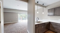 This well-appointed three-bedroom, three-bathroom home spans three floors, offering a functional and comfortable layout across generous living areas. The main floor features an open-concept kitchen and living room combination, where dark espresso cabinetry, white countertops, and stainless steel appliances—including a full-size refrigerator—give the kitchen a clean, modern aesthetic. Stylish pendant lighting hangs above the sink area, adding a refined touch. The adjacent living room is bathed in natural light from large sliding glass doors that open to views of mature trees and a fenced outdoor area, creating a seamless indoor-outdoor connection. Soft, plush carpeting flows throughout the living and bedroom spaces, adding warmth and comfort underfoot. The spacious primary bedroom on the upper floor offers a ceiling fan with light fixture and a bright window overlooking the neighborhood. Additional bedrooms are well-sized, each featuring carpeted floors, neutral wall tones, and closet storage with built-in racking systems. All three bathrooms are finished with dark-hardware fixtures, wide vanity mirrors, white countertops, and dark wood cabinetry. A tub-shower combo with tiled surround is present in one bathroom. The overall design palette of warm neutrals and consistent finishes gives the entire home a cohesive, move-in-ready feel.