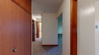 Located at 1063 Halstead Dr in Cortland, NY, this single-floor, three-bedroom, one-bathroom home offers a practical and well-organized layout. Warm wood trim and baseboards accent the neutral-toned walls throughout, providing a cohesive aesthetic across the home.

The kitchen is efficiently designed, featuring rich wood cabinetry with ample upper and lower storage, a white electric range, refrigerator, and a double basin sink. A charming bay window floods the kitchen dining area with natural light and offers pleasant views of the surrounding greenery.

The spacious primary bedroom is carpeted and benefits from a large multi-pane window overlooking the outdoors, along with baseboard heating. A doorway leads to a walk-in closet area with wood-paneled storage. The two additional bedrooms are also carpeted with neutral walls, windows, and built-in closet space, each serviced by baseboard heating for year-round comfort.

A central hallway connects all rooms, finished with carpet and warm wood door frames. The bathroom includes a tub and shower combination with a sliding glass enclosure, tiled surround, and a standard vanity. Throughout the home, consistent warm-toned wood accents and soft carpet flooring create a comfortable, move-in-ready living environment.