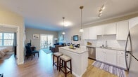 Located at 9 Covered Bridge Road, this 1-bedroom, 1-bathroom residence is thoughtfully designed across a single floor, offering a cohesive open-concept layout that maximizes every square foot. The kitchen serves as a central highlight, featuring crisp white shaker cabinetry, granite countertops, a classic subway tile backsplash, stainless steel appliances, and a center island with bar seating — ideal for casual dining or entertaining. Pendant lighting and track fixtures add warm, layered illumination throughout. Durable wood-look flooring extends seamlessly from the kitchen into the living area, which is filled with natural light and anchored by sliding glass doors that open to a private balcony with views of surrounding trees. The bedroom is a calm retreat, offering a closet, natural light from a large window, and neutral tones throughout. The full bathroom features a dark wood vanity with a white countertop, a large mirror, crown molding, and a tub/shower combination. Crown molding accents the kitchen and bathroom, adding an elevated finish to the overall design. The space blends modern convenience with comfortable, everyday livability.