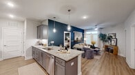 Located at 7100 Summerside Dr in Whitsett, NC, this single-story, 2-bedroom, 2-bathroom home offers a thoughtfully designed open-concept layout with modern finishes and cohesive style throughout. The kitchen and living area flow seamlessly together, anchored by a striking deep teal accent wall that adds bold character to the space. The kitchen is equipped with gray shaker-style cabinetry, granite countertops, stainless steel appliances including a dishwasher and range, a double-basin sink, and elegant pendant lighting above the central island. Light hardwood flooring extends throughout, enhancing the bright, airy atmosphere. The living area features a ceiling fan and a glass-paneled exterior door that invites natural light and outdoor access. The primary bedroom continues the teal accent wall motif, creating a sophisticated and restful retreat, while the second bedroom offers a clean, neutral palette with a ceiling fan. Both bathrooms are finished with granite counters and wood-look flooring; one features a glass-enclosed walk-in shower. A dedicated laundry room houses a full-size washer and dryer with overhead wire shelving for added storage. This home combines practical functionality with refined design details for comfortable everyday living.