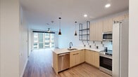 Located at 945 Mid City Drive in Huntsville, AL, this modern one-bedroom, one-bathroom unit offers a well-designed open-concept layout that seamlessly connects the kitchen, dining, and living areas. The kitchen is a standout feature, showcasing light wood cabinetry, a peninsula with a built-in sink and stainless steel dishwasher, a stainless steel range and refrigerator, a tile backsplash with a geometric pattern, open industrial-style shelving, and stylish pendant lighting. Recessed lighting and wood-style flooring run throughout the main living area, adding warmth and continuity to the space. Large floor-to-ceiling windows in the living area and bedroom flood the unit with natural light and frame views of the surrounding urban streetscape. The bedroom is a comfortable size, equipped with a ceiling fan, wood-style flooring, and access to a dedicated walk-in closet with built-in shelving and a hanging rod. The bathroom features a clean, minimalist design with a soaking tub and shower combo, tile surround, and a wood-toned vanity with a stone countertop. Overall, the unit offers a cohesive modern aesthetic with quality finishes throughout.