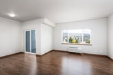 This single-floor unit offers a thoughtfully designed layout that balances open living spaces with functional private areas. The living room is a standout feature, bathed in natural light from a large picture window that frames expansive cityscape and mountain views. A sliding glass door provides direct access to an outdoor space, further enhancing the bright, airy ambiance. Rich hardwood-style flooring extends throughout, complemented by warm-toned baseboards and neutral wall colors that create a clean, welcoming atmosphere.

The kitchen is equipped with white flat-panel cabinetry extending to the ceiling, light-toned countertops, and a full suite of stainless steel appliances, including a refrigerator, electric range, built-in microwave, and dishwasher. A hallway connects the main living areas to the private spaces, lined with warm wood-toned doors that add a distinctive design element. The bedroom features carpeted flooring and its own window for natural light. The bathroom is finished with durable flooring, a walk-in shower enclosed by frosted glass sliding doors, and a small window for ventilation. The overall design is modern and practical, offering a comfortable and cohesive living environment.
