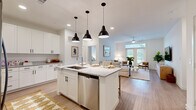 This thoughtfully designed 2-bedroom, 2-bathroom residence in Austin, TX features a clean, modern aesthetic throughout its single-story open-concept layout. The kitchen serves as a focal point of the home, showcasing white shaker cabinetry, granite countertops, stainless steel appliances—including a French door refrigerator, range, and built-in microwave—and a large center island with an undermount sink and seating for multiple guests, illuminated by three bold black pendant lights. Light wood-tone flooring runs throughout the main living areas, lending warmth and continuity. The adjoining living room is generously proportioned, featuring a ceiling fan, large windows with French doors that invite abundant natural light and outdoor views, creating a bright and welcoming atmosphere. Both bedrooms are comfortably sized, each benefiting from natural light, and are accompanied by dedicated closets. The primary bedroom connects to its own bathroom, which features granite-topped white cabinetry, a framed mirror, and open shelving. The second bathroom mirrors the same refined finishes. Together, the spaces deliver a cohesive, contemporary feel well-suited to modern living in the heart of Austin.