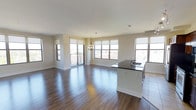 This well-appointed 2-bedroom, 2-bathroom residence offers a thoughtfully designed single-floor layout that maximizes both space and comfort. The open-concept living and kitchen area is the heart of the home, anchored by rich hardwood flooring that flows seamlessly throughout the main living space. Large windows on multiple walls flood the interior with abundant natural light, creating a bright and airy ambiance at all hours of the day. A sliding glass door leads to a private balcony, offering elevated outdoor views and additional ventilation. The kitchen features a sleek island with a dark granite countertop and an integrated sink, providing both a functional workspace and a casual gathering spot. A classic chandelier adds an elegant focal point above the dining area, complementing the clean, neutral-toned walls and white baseboards. The overall design aesthetic is modern yet understated, with a neutral color palette that lends itself to a variety of décor styles. The generous square footage ensures comfortable living across both bedrooms and bathrooms, making this residence an ideal choice for those seeking a balance of style, functionality, and natural light in a well-proportioned floor plan.