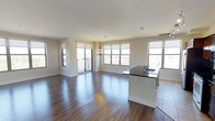 This well-appointed 2-bedroom, 2-bathroom residence offers a thoughtfully designed single-floor layout that maximizes both space and comfort. The open-concept living and kitchen area is the heart of the home, anchored by rich hardwood flooring that flows seamlessly throughout the main living space. Large windows on multiple walls flood the interior with abundant natural light, creating a bright and airy ambiance at all hours of the day. A sliding glass door leads to a private balcony, offering elevated outdoor views and additional ventilation. The kitchen features a sleek island with a dark granite countertop and an integrated sink, providing both a functional workspace and a casual gathering spot. A classic chandelier adds an elegant focal point above the dining area, complementing the clean, neutral-toned walls and white baseboards. The overall design aesthetic is modern yet understated, with a neutral color palette that lends itself to a variety of décor styles. The generous square footage ensures comfortable living across both bedrooms and bathrooms, making this residence an ideal choice for those seeking a balance of style, functionality, and natural light in a well-proportioned floor plan.