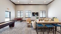 Located at 2230 S Ellis Rd in Sioux Falls, South Dakota, this single-story community amenity space is thoughtfully designed to serve residents with a comprehensive range of shared facilities. The layout encompasses several distinct areas, each tailored to a specific function while maintaining a cohesive aesthetic throughout.

The communal kitchen features white shaker-style cabinetry with matte black hardware, dark countertops, stainless steel appliances including a range and refrigerator, and luxury vinyl plank flooring. Soaring ceilings and a pendant light add an elevated feel to this functional space.

The main gathering lounge boasts dramatically high ceilings with rich crown molding, large windows allowing ample natural light, patterned carpeting, and a wall-mounted television. Comfortable seating, high-top tables, a foosball table, and a shuffleboard table make it ideal for socializing and recreation.

A dedicated media room offers plush seating, recessed lighting, and film reel wall décor, creating a cozy cinema-inspired atmosphere. Adjacent spaces provide additional lounge seating with a mounted television for quieter gatherings.

The expansive fitness center is divided into multiple zones accommodating cardio equipment—including treadmills, stationary bikes, and ellipticals—as well as strength training with a cable machine, adjustable bench, and dumbbell rack. Large windows provide natural light throughout the workout areas.