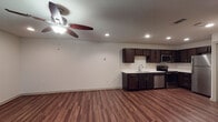 This single-floor unit offers a clean, modern interior designed for comfortable everyday living. Rich, dark hardwood-style flooring runs throughout the main living areas, creating a warm and cohesive aesthetic from room to room.

The open living area is bright and welcoming, featuring recessed lighting and a ceiling fan with light fixture that provides both comfort and illumination. A window dressed with blinds allows natural light to filter into the space, adding to its airy feel.

The kitchen is well-equipped and thoughtfully designed, showcasing dark espresso-toned cabinetry that extends to the ceiling for ample storage. Crisp white countertops provide a striking contrast, and the space is outfitted with a full suite of stainless steel appliances, including a refrigerator, electric range, over-the-range microwave, and dishwasher. A double-basin stainless steel sink with a modern pull-down faucet completes the functional layout.

The bathroom maintains the same dark cabinetry and white countertop combination seen in the kitchen, ensuring a consistent design language throughout the unit. It features a full tub and shower combination with neutral tile surround, a toilet, and a vanity with under-sink storage.

Overall, the unit presents a cohesive and practical living environment with durable finishes, modern fixtures, and a neutral color palette that offers a versatile backdrop for any style of décor.