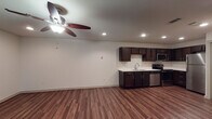 This single-floor unit offers a clean, modern interior designed for comfortable everyday living. Rich, dark hardwood-style flooring runs throughout the main living areas, creating a warm and cohesive aesthetic from room to room.

The open living area is bright and welcoming, featuring recessed lighting and a ceiling fan with light fixture that provides both comfort and illumination. A window dressed with blinds allows natural light to filter into the space, adding to its airy feel.

The kitchen is well-equipped and thoughtfully designed, showcasing dark espresso-toned cabinetry that extends to the ceiling for ample storage. Crisp white countertops provide a striking contrast, and the space is outfitted with a full suite of stainless steel appliances, including a refrigerator, electric range, over-the-range microwave, and dishwasher. A double-basin stainless steel sink with a modern pull-down faucet completes the functional layout.

The bathroom maintains the same dark cabinetry and white countertop combination seen in the kitchen, ensuring a consistent design language throughout the unit. It features a full tub and shower combination with neutral tile surround, a toilet, and a vanity with under-sink storage.

Overall, the unit presents a cohesive and practical living environment with durable finishes, modern fixtures, and a neutral color palette that offers a versatile backdrop for any style of décor.