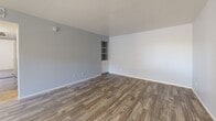Located at 350 N Harrison Rd in Tucson, Arizona, this 2-bedroom, 2-bathroom single-floor home offers a practical and comfortable layout. The living room sets a welcoming tone with cool gray walls, wood-look plank flooring, and a built-in shelving unit with cabinet storage — a functional and distinctive architectural detail. A front entry door opens directly into this main living area, which flows into a well-proportioned hallway connecting the rest of the home. The galley-style kitchen is outfitted with white cabinetry, light stone-look countertops, and white appliances including a range, refrigerator, and dishwasher, all set over matching wood-look flooring. The primary bedroom features plush carpeting, a ceiling fan with light fixture, and sliding glass doors that open to a private balcony — a standout feature offering outdoor access and natural light. The second bedroom also includes carpeting and a ceiling fan, providing a comfortable and functional space. Both bathrooms continue the wood-look flooring theme; one includes a walk-in glass-door shower with a vanity and stone-look countertop, while the other features a full shower-tub combination. A dedicated closet provides additional storage. The home presents a clean, neutral palette throughout.