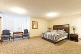 Located at 1477 Mississauga Valley Blvd, this well-appointed one-bedroom, one-bathroom suite offers a thoughtfully organized layout across a single floor. The generously sized bedroom serves as the heart of the suite, featuring warm patterned carpeting, striped wallpaper, and soft ambient lighting from ceiling fixtures and bedside lamps. A dark-wood queen bed with matching nightstands anchors the space, while a dedicated sitting area with two armchairs and a small table sits beside a large window dressed with vertical blinds, allowing natural light to filter in. A wall-mounted air conditioning unit and a dresser with a flat-screen television complete the bedroom's functional offerings. Framed artwork adds a welcoming, residential touch throughout.

The kitchenette is efficiently designed with white cabinetry extending to the upper walls, a double-basin sink, a compact refrigerator, and countertop appliances including a microwave and coffee maker — all set on light tile flooring. The full bathroom features a tub and shower combination with a curtain, a toilet, and a vanity with a granite-style countertop and integrated sink, all finished in clean white tile. This suite offers a practical and comfortable living environment with all essential amenities within a compact, well-utilized footprint.