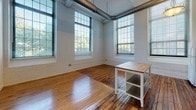 Located at 166 Valley St in Providence's West End, this single-floor loft-style unit blends industrial character with modern functionality. The space showcases rich, original hardwood floors throughout, complemented by crisp white walls and exposed painted brick that speak to the building's historic mill origins.

The open living and dining area is a standout, featuring soaring ceilings with exposed ductwork and an abundance of natural light pouring in through oversized, multi-pane factory-style windows. These generous windows frame views of the surrounding neighborhood and lend the space an airy, expansive feel.

The kitchen is efficiently laid out and equipped with light wood cabinetry, a gas range, refrigerator, dishwasher, and a double sink with ample counter space. A butcher block island provides additional prep and storage options.

A bright, well-lit hallway connects the main living areas to the additional rooms, which continue the hardwood flooring and white wall aesthetic, with large windows bringing in natural light. The bathroom is cleanly finished with tile flooring, a pedestal sink, toilet, and a stand-up shower. Recessed lighting throughout the hallway and main areas adds a polished touch to this characterful, industrial-inspired space.