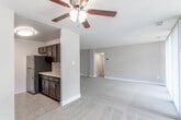 This single-floor residence offers a well-organized layout with a seamless flow between its main living spaces. The open living and dining area is finished with neutral-toned carpet and painted in warm beige tones, creating a bright and inviting atmosphere. A ceiling fan with a light fixture is centrally positioned, providing both airflow and ambient lighting. Built-in shelving near a closet adds practical storage directly within the living space.

The galley-style kitchen is efficiently designed with rich dark espresso cabinetry lining both walls, light-toned countertops, and tile flooring. It is equipped with stainless steel appliances, including a gas range, microwave, and refrigerator, along with a stainless steel sink. The kitchen connects conveniently to the main living area via a partial wall with counter space.

The bedroom is generously proportioned with soft carpeting and neutral walls, and features access to a walk-in closet with interior lighting. A window fitted with vertical blinds allows natural light while maintaining privacy. The bathroom includes a full tub and shower combination with white tile surround. A sliding glass door in the living area opens to an outdoor balcony with views of mature trees, bringing in natural light and greenery.