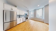 Located at 101 South Salina Street in the heart of downtown Syracuse, NY, this single-floor unit offers a thoughtfully designed layout with contemporary finishes throughout. The open-concept kitchen and living area serves as the centerpiece of the space, showcasing warm hardwood flooring that extends seamlessly throughout. The kitchen is outfitted with white shaker-style cabinetry, a soft gray subway tile backsplash, light quartz countertops, and a full suite of stainless steel appliances including a refrigerator, range, microwave, and dishwasher. A matte black gooseneck faucet adds a modern accent to the undermount sink. Large floor-to-ceiling windows flood the living area with natural light while offering views of the surrounding downtown Syracuse streetscape. Track lighting and recessed fixtures provide additional illumination throughout. A dedicated bedroom features the same hardwood flooring, a large window with urban views, and clean white walls that create a bright, neutral canvas. The bathroom is finished with large-format tile flooring, a white vanity with an undermount sink, and a glass-enclosed walk-in shower with marble-style tile surround and brushed nickel hardware. The overall aesthetic is clean, modern, and move-in ready, making this space well-suited for urban living in one of Syracuse's most accessible locations.