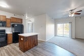 Located at 6000 NW 106th St in Johnston, Iowa, this three-bedroom, two-bathroom single-floor home offers a well-designed layout with comfortable, functional living spaces throughout. The combined kitchen and living area serves as the heart of the home, featuring vaulted ceilings, wood-tone luxury vinyl plank flooring, and a ceiling fan that enhances airflow and ambiance. A sliding glass door floods the living area with natural light and provides direct access to the outdoors. The kitchen is appointed with rich walnut-toned cabinetry, a light countertop island with pendant lighting, a full suite of black appliances including a refrigerator, range, dishwasher, and built-in microwave, plus a double sink beneath under-cabinet lighting. Each of the three bedrooms is carpeted for comfort and includes a closet — the primary bedroom features a spacious walk-in closet with wire shelving. The two bathrooms are finished with warm wood cabinetry, white countertops, and luxury vinyl plank flooring; one includes a full tub/shower combo. A dedicated laundry room with side-by-side washer and dryer hookups adds everyday convenience. The hallway connects all rooms efficiently, with additional utility and storage closets rounding out the home's practical layout.
