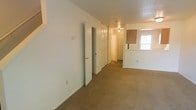 This two-floor residential space offers a straightforward and functional layout designed for comfortable everyday living. The main level features wall-to-wall carpeting throughout, lending a warm and quiet atmosphere to the living and hallway areas. A generously sized hallway runs through the heart of the space, lined with multiple closet doors that provide ample built-in storage solutions. The white walls and neutral tones create a clean, bright backdrop that makes the interior feel open and easy to personalize. Ceiling-mounted light fixtures illuminate the corridor and adjoining areas, ensuring consistent lighting throughout. At the end of the hallway, a kitchen area comes into view, distinguished by a pass-through window that connects it to the adjacent living space — a practical feature that promotes an open feel between the cooking and living zones. A window in the kitchen area allows natural light to filter in, brightening the space. The two-floor configuration offers separation between living and private areas, adding a sense of depth and versatility to the overall floor plan. The space presents a neutral, move-in-ready canvas well-suited for a variety of living arrangements.