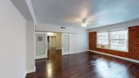 Located at 6500 Yucca St in the heart of Hollywood, Los Angeles, this single-story unit blends classic character with functional design. The main living area immediately draws attention with its richly stained hardwood floors that run throughout the space, a ceiling fan overhead, and a striking exposed brick accent wall that adds warmth and texture. Natural light filters in through large windows, brightening the open layout. A standout architectural feature is the pair of frosted glass sliding barn doors, which provide flexible separation between the living area and the adjoining rooms while maintaining an airy, connected feel. The bedroom is well-proportioned, continuing the hardwood flooring and offering a mirrored sliding closet for storage. The bathroom is clean and straightforward, featuring a full tub-shower combination, a single vanity with sink, and wood-look flooring. The kitchen is efficiently laid out with white cabinetry offering ample storage, light stone-look countertops, a gas range, and a refrigerator. Together, these elements create a cohesive living environment that balances vintage charm — evident in the brick detailing and classic hardwood — with practical, updated finishes throughout.