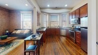 This single-floor space masterfully blends industrial character with modern comfort. Exposed brick walls are a defining architectural feature throughout, lending warmth and texture to nearly every room. Rich hardwood flooring runs continuously across the open layout, tying the spaces together cohesively.

The open-concept kitchen and living area forms the heart of the unit. The kitchen is well-appointed with rich cherry wood cabinetry, granite-style countertops, stainless steel appliances including a dishwasher, microwave, and range, and a double basin sink set beneath a curved bay of windows that floods the space with natural light. A granite-topped bar-height table with seating bridges the kitchen and living area seamlessly.

The living area features exposed brick accent walls and large windows that invite abundant natural light. The bedroom is a standout, with soaring exposed brick walls on multiple sides and visible industrial ductwork that reinforces the loft aesthetic. A secondary room with exposed brick and a large window offers flexible use as an additional bedroom or lounge. Two full bathrooms, each with a tub-shower combination and cherry wood vanities, provide practical functionality. The overall ambiance is urban and characterful, balancing historic architectural elements with contemporary finishes.
