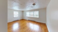 Located in the Germantown neighborhood of Philadelphia, this single-floor unit at 330 W Johnson Street offers a clean, functional layout with consistent design details throughout. Warm hardwood flooring runs through the main living areas and bedrooms, lending a classic character to the space. The living room is spacious and bright, featuring large multi-pane windows that invite generous natural light and views of the surrounding neighborhood. Baseboard heating is present throughout, ensuring year-round comfort. A second bedroom or bonus room features a charming corner window arrangement, further maximizing light and providing an airy feel. The kitchen is well-equipped with warm wood cabinetry, a gas range, a refrigerator, a double sink, and tile backsplash, all centered around a bright window overlooking greenery outside. Tile flooring in the kitchen provides a practical contrast to the hardwood elsewhere. The bathroom stands out with fully tiled walls in a neutral earth tone, a modern rain showerhead with a handheld attachment, and a window for natural ventilation. The overall ambiance of the unit is bright, clean, and functional, with a straightforward layout that makes efficient use of the available space.