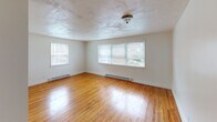 Located in the Germantown neighborhood of Philadelphia, this single-floor unit at 330 W Johnson Street offers a clean, functional layout with consistent design details throughout. Warm hardwood flooring runs through the main living areas and bedrooms, lending a classic character to the space. The living room is spacious and bright, featuring large multi-pane windows that invite generous natural light and views of the surrounding neighborhood. Baseboard heating is present throughout, ensuring year-round comfort. A second bedroom or bonus room features a charming corner window arrangement, further maximizing light and providing an airy feel. The kitchen is well-equipped with warm wood cabinetry, a gas range, a refrigerator, a double sink, and tile backsplash, all centered around a bright window overlooking greenery outside. Tile flooring in the kitchen provides a practical contrast to the hardwood elsewhere. The bathroom stands out with fully tiled walls in a neutral earth tone, a modern rain showerhead with a handheld attachment, and a window for natural ventilation. The overall ambiance of the unit is bright, clean, and functional, with a straightforward layout that makes efficient use of the available space.