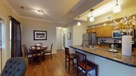 This single-floor residence offers a thoughtfully designed layout that balances functionality and comfort across its living spaces. The kitchen serves as a central highlight, featuring warm honey-toned cabinetry, dark granite countertops, and a full suite of stainless steel appliances including a refrigerator, range, and built-in microwave. A peninsula with an integrated double sink and bar-height seating creates a natural transition between the kitchen and the adjacent dining area, where pendant lighting adds an inviting ambiance. The dining space accommodates a round table with seating for multiple guests and benefits from natural light filtering through drapery-framed windows.

The bedroom is generously proportioned, with hardwood-style flooring, crown molding, and ample natural light from a windowed wall dressed in sheer curtains. A secondary bedroom nook provides a quieter, more intimate retreat with soft carpeting and warm lighting. The bathroom is well-equipped with a dual-sink vanity topped in white countertops, wood cabinetry, a full soaking tub, and tile flooring throughout. Neutral wall tones and crown molding details unify the interior, lending the overall space a cohesive and polished character.